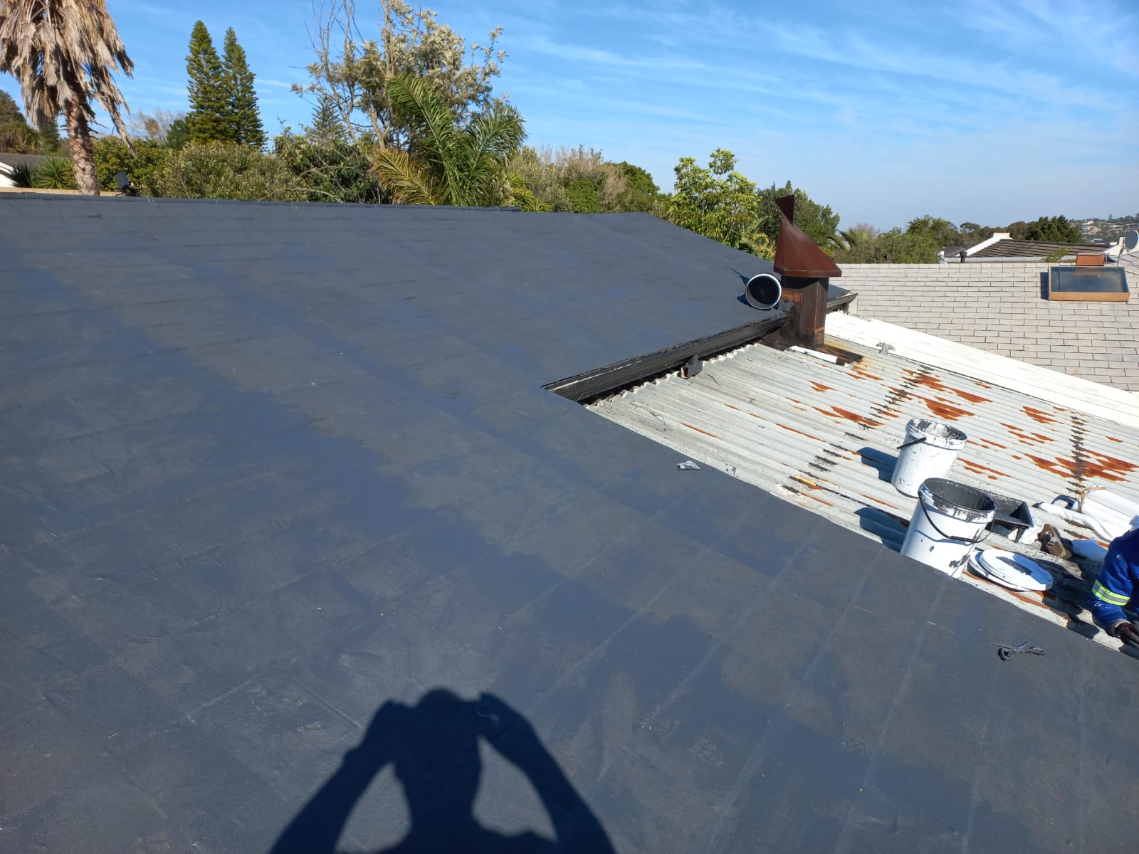Torch-on membrane laid over a low-pitch roof beside the original rusted sheeting